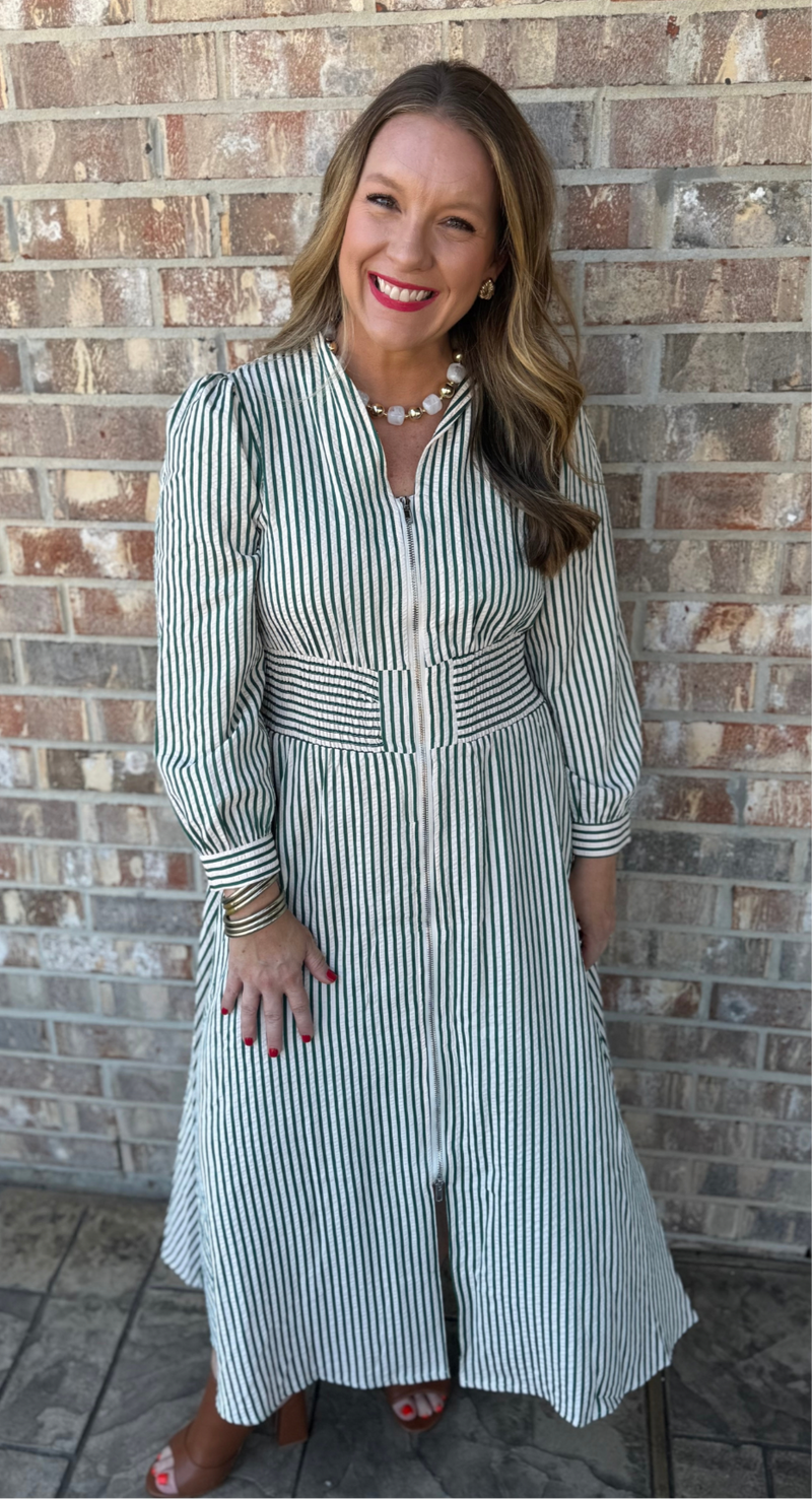 Woman wearing a striped dress standing against a brick wall.