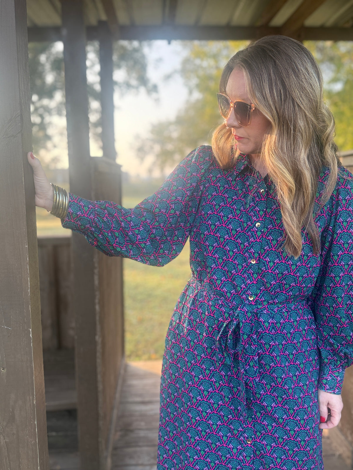 Woman in a blue patterned dress standing outdoors near a wooden structure.
