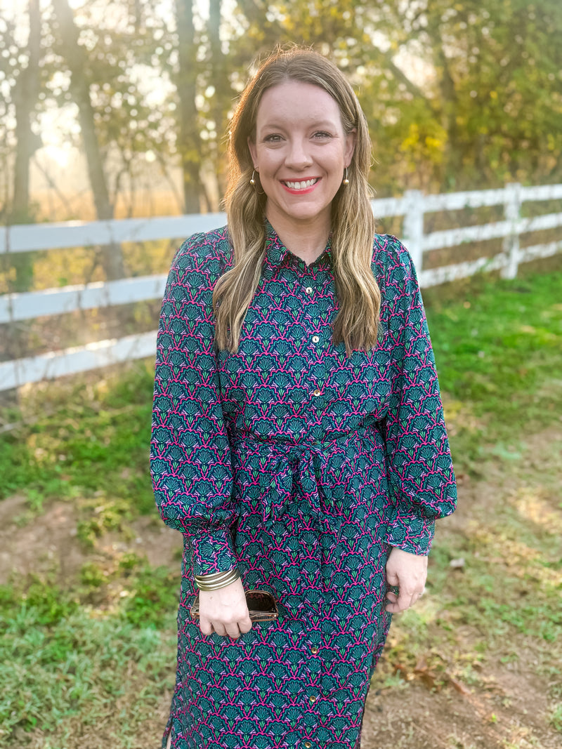 Woman wearing a patterned dress standing outdoors with a white fence and trees in the background